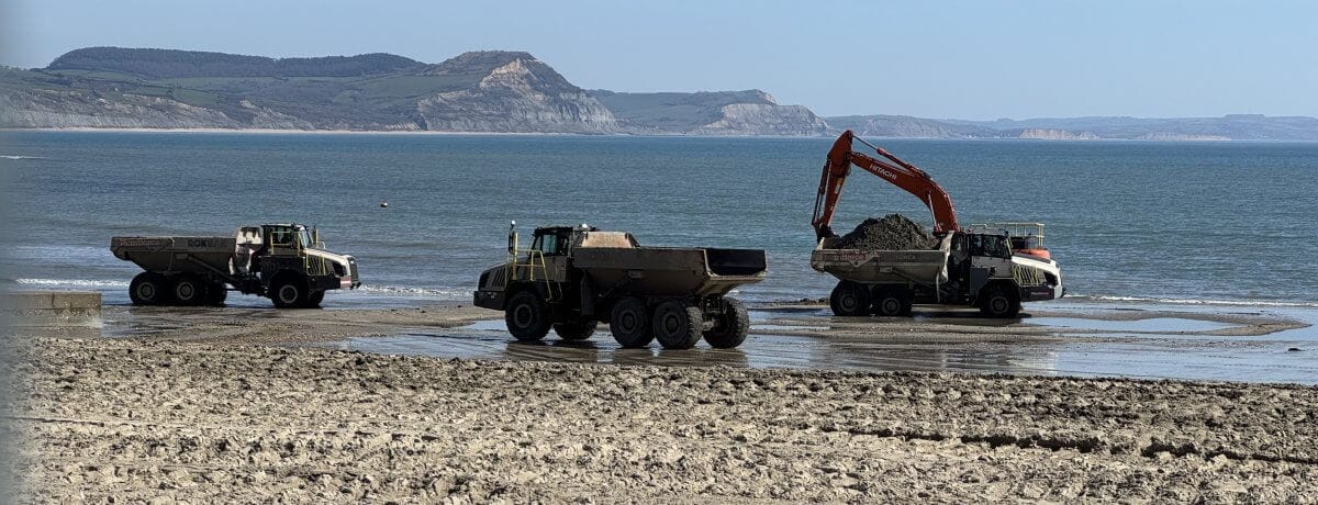 Diggers moving sand on Lyme Regis sandy beach after winter storm